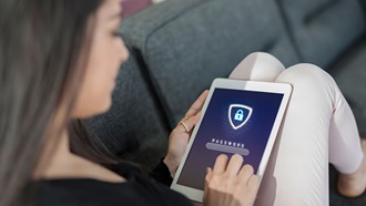 Een vrouw die op haar bank zit, kijkt naar haar tablet.
